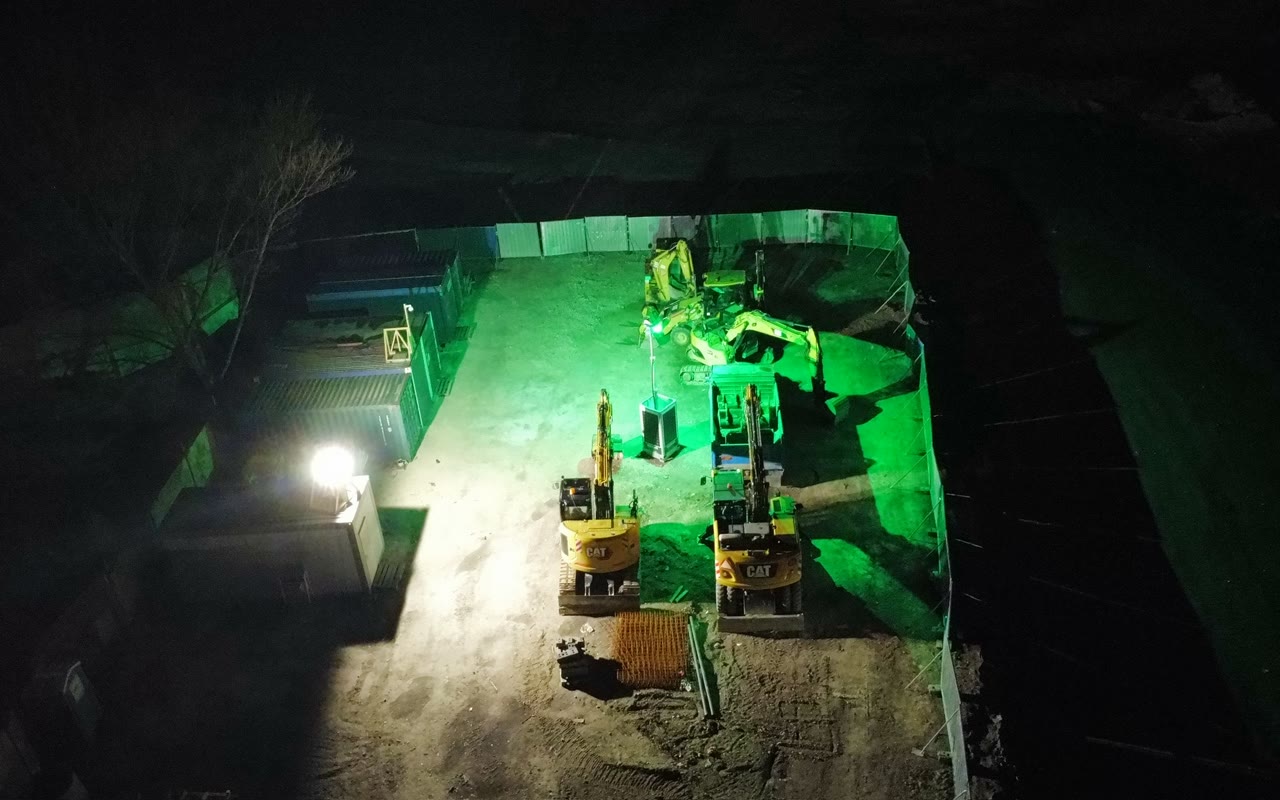 Stavenisko v noci z dronu, osvetlené zeleným svetlom veže SERAF